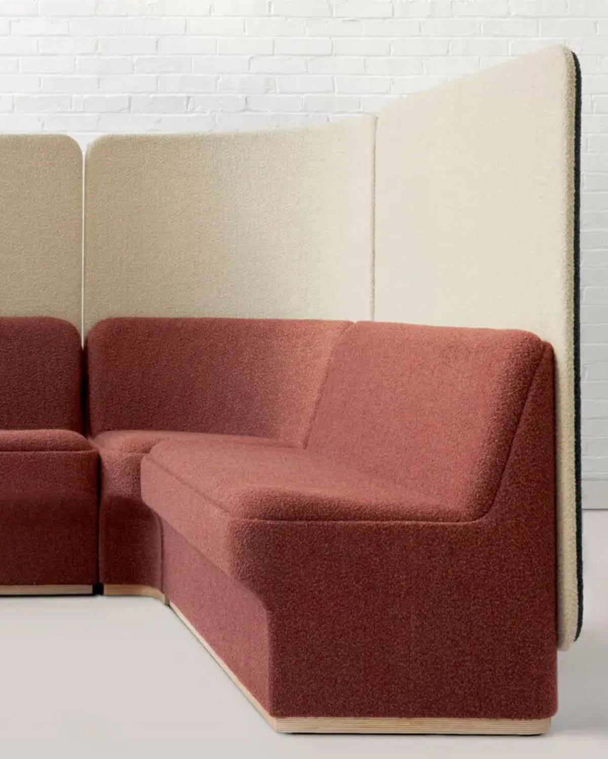 A modern modular upholstered seating unit with a terracotta red fabric seat and back, paired with light beige fabric privacy panels, shown in a minimalist room setting.