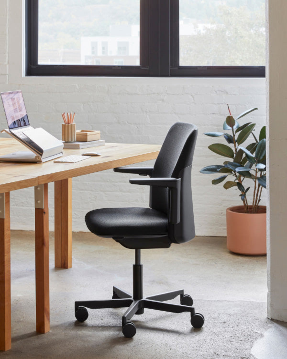Modern office setup with a wooden desk, black office chair, and a plant.