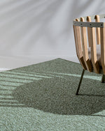 Green textured rug with a wooden chair casting a shadow on it