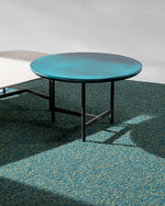 Round turquoise table with black legs on a textured green floor.