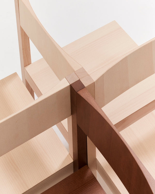 Close-up of a wooden furniture corner showing light natural wood and darker reddish-brown wood pieces joined together with a visible mortise and tenon joint.