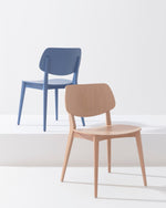 Two modern dining chairs on a clean white studio background: a natural wood chair in the foreground and a blue chair behind it on a raised platform.
