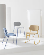 Three modern accent chairs in blue, gray, and beige with metal frames, arranged on white platform steps against a minimalist white studio background.
