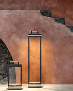 Carre XL Floor Lamp and Table Lamp in a rustic room, the XL lamp lighting up the wall behind with its warm light.
