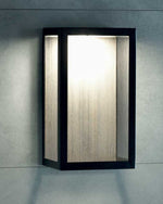 Carre Wall Lamp in sepia black and pickled teak, lit up and hanging off of wall.