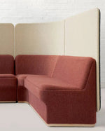 A modern modular upholstered seating unit with a terracotta red fabric seat and back, paired with light beige fabric privacy panels, shown in a minimalist room setting.