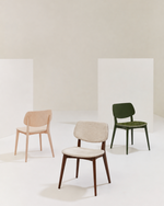 Three modern dining chairs displayed in a minimalist studio setting: a light wood chair with a beige seat on the left, a central chair with a dark brown wood frame and light beige upholstered seat, and a dark green chair with a green upholstered seat on the right.