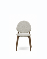 A modern dining chair with a textured light beige bouclé upholstered seat and rounded backrest, supported by four tapered dark brown wooden legs, shown against a plain white background.
