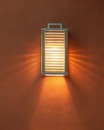 Ginger Wall Lamp hanging and lit up with light hitting the orange wall behind it. 