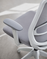 A close-up of a modern office chair with a light gray fabric seat and backrest, a white frame, and a matching gray armrest, shown in a minimalist indoor setting.