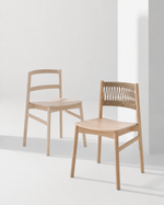 Two light natural wood dining chairs in a minimalist studio setting with a white wall and floor, casting soft shadows.