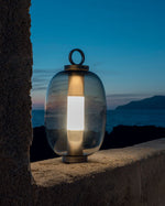Lucerna Outdoor Lamp perched on a wall, in the background is the sea.