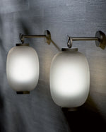 Lucerna Suspension Lamp in aluminium towards the front, and brass-plated aluminium in the background both with white lights inside.