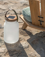 Milk solar lamp outdoors charging in the sunlight, placed on a stone pathway and next to a lounge chair.
