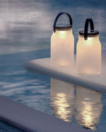Two milk solar lamps by the pool, lit up as the sun sets and it turns to dusk.