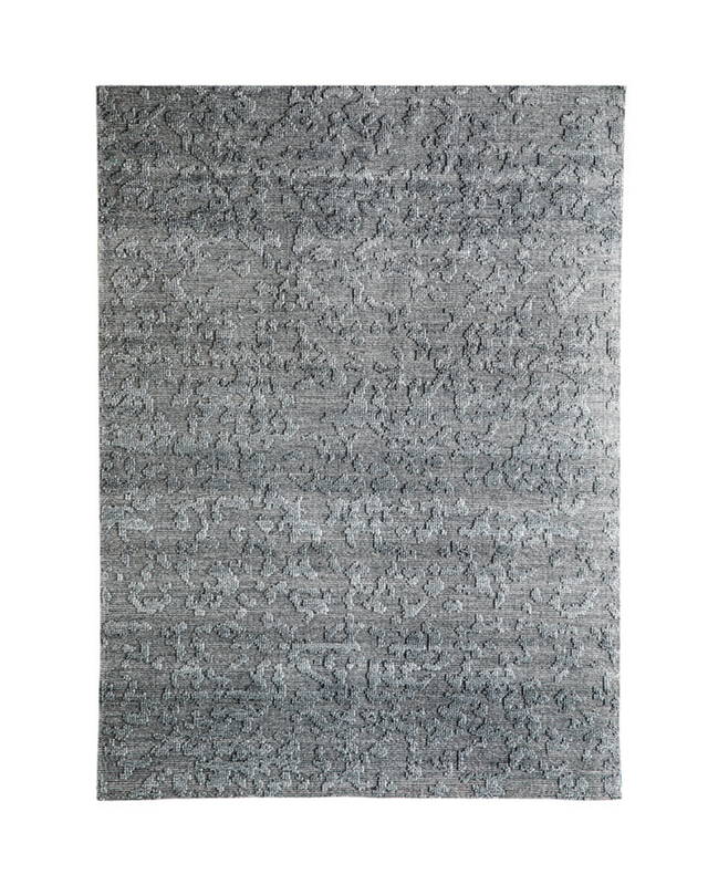 A rectangular area rug with a textured, abstract pattern in shades of gray and silver, shown flat against a white background.