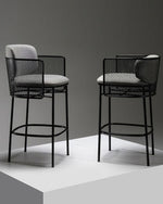 Two black bar stools with woven backrests and white cushioned seats on a gray background.
