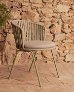 Chair with woven backrest and cushioned seat against a stone wall.