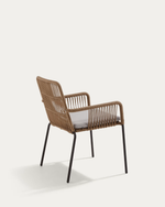 A modern outdoor armchair with a woven brown wicker frame, black metal legs, and a light gray cushion, shown from a three-quarters angle against a solid off-white background.
