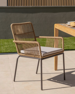 Rattan chair with a cushion on a patio area with a table in the background.
