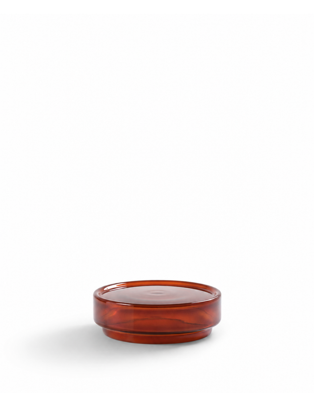 A small round amber-brown translucent glass dish or candle holder with a smooth glossy finish, set against a solid white background.