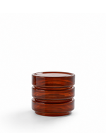 A small amber-brown translucent glass cup with a stacked, ribbed design, photographed on a clean white background.