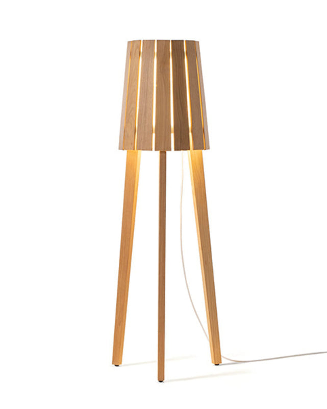 Woody Floor Lamp in natural teak wood, with the light on and a cord reaching the floor from the inside of the lamp head.