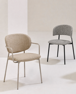 Two modern dining chairs in a minimalist studio setting. The foreground chair features a light beige textured fabric upholstery with a light gray metal frame.